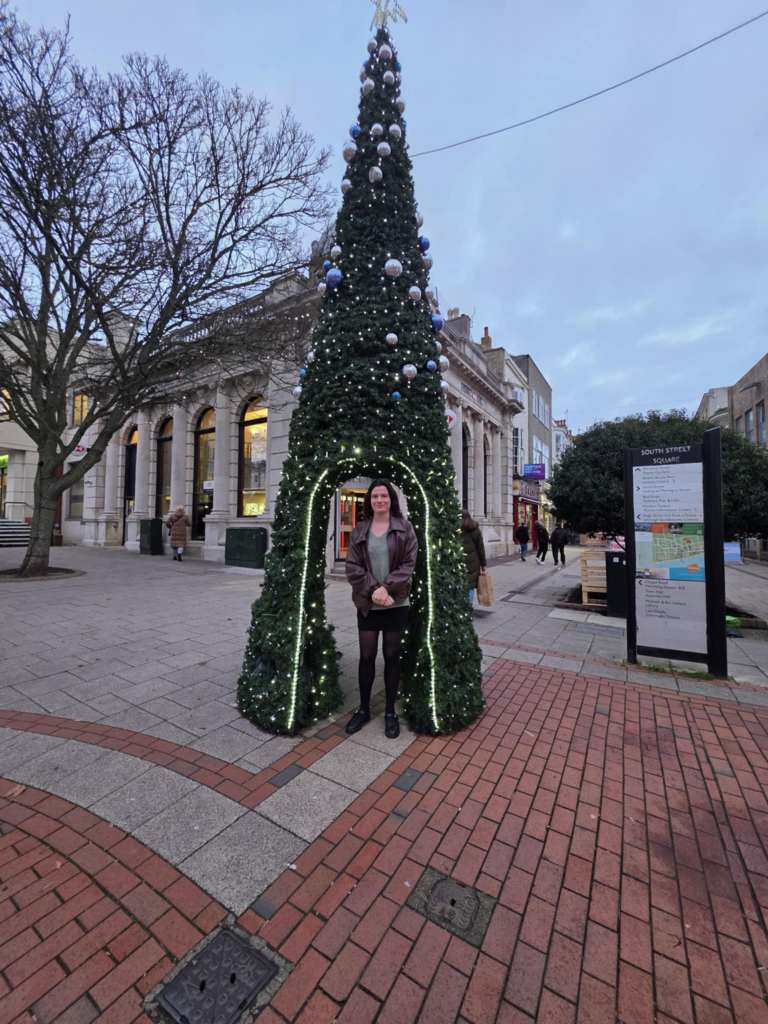 Person stood underneath a Christmas tree in the street.